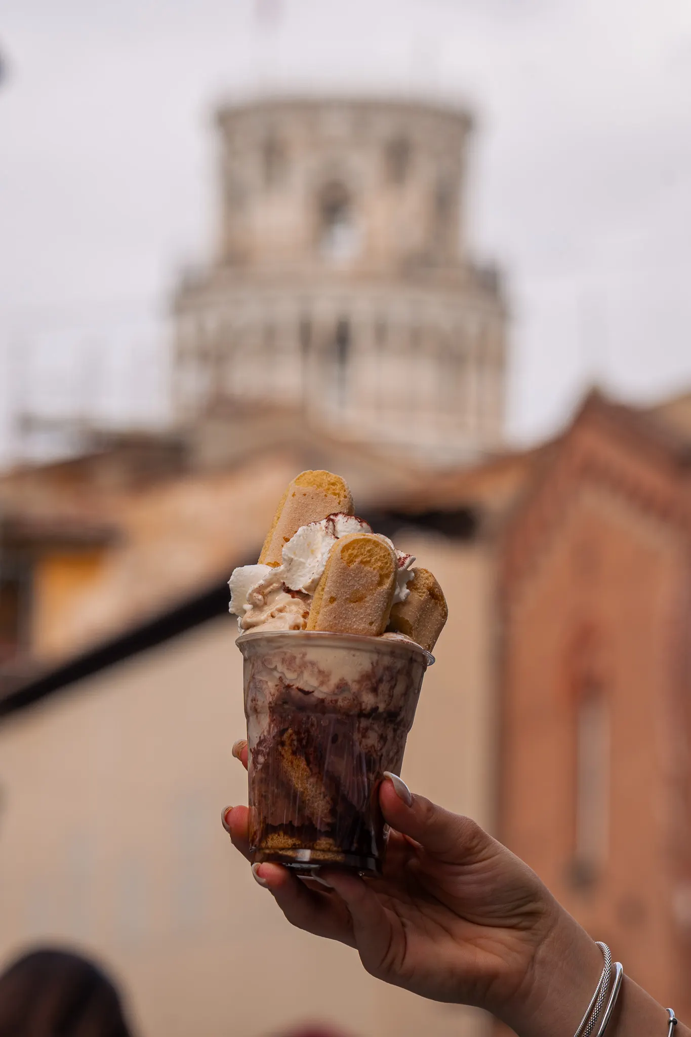Coppa di gelato con panna e biscotti tenuta in mano davanti alla Torre di Pisa