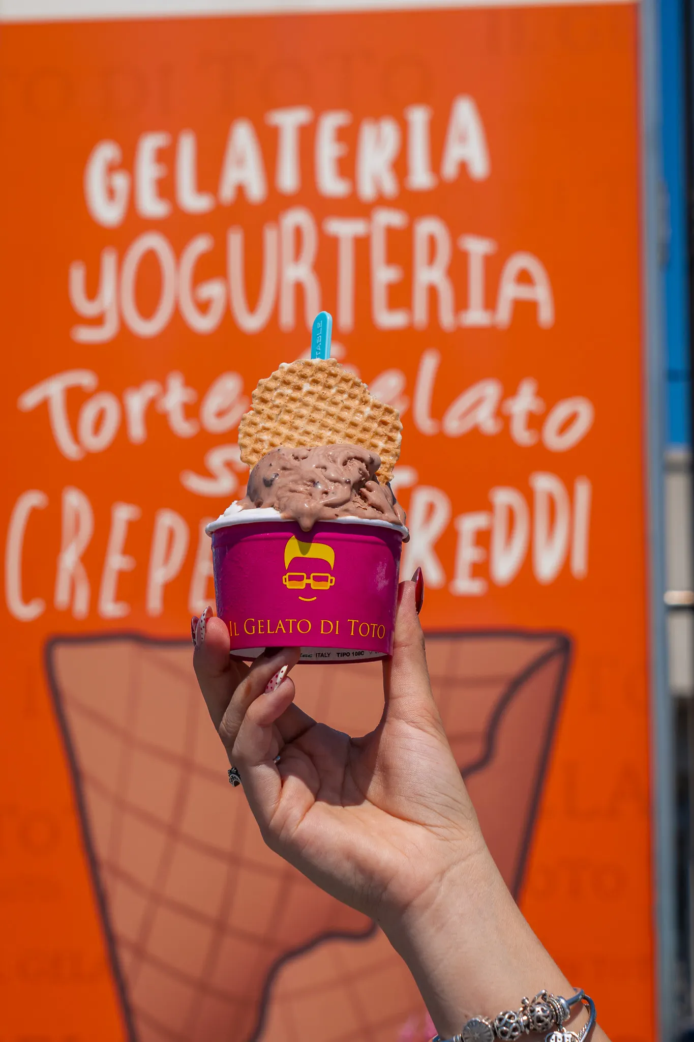 Coppetta magenta di Toto davanti al cavalletto arancione della gelateria