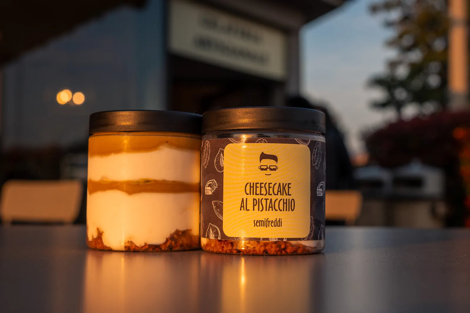 Due vasetti di cheesecake al pistacchio davanti all'ingresso della gelateria